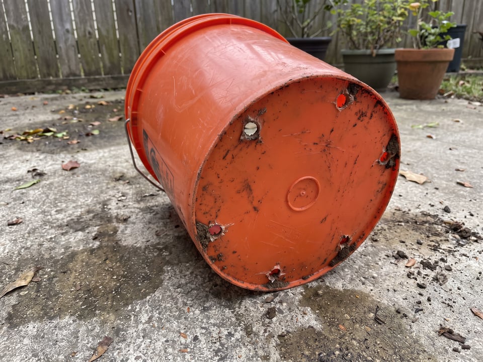 The underside of a 5-gallon bucket with drilled drainage holes