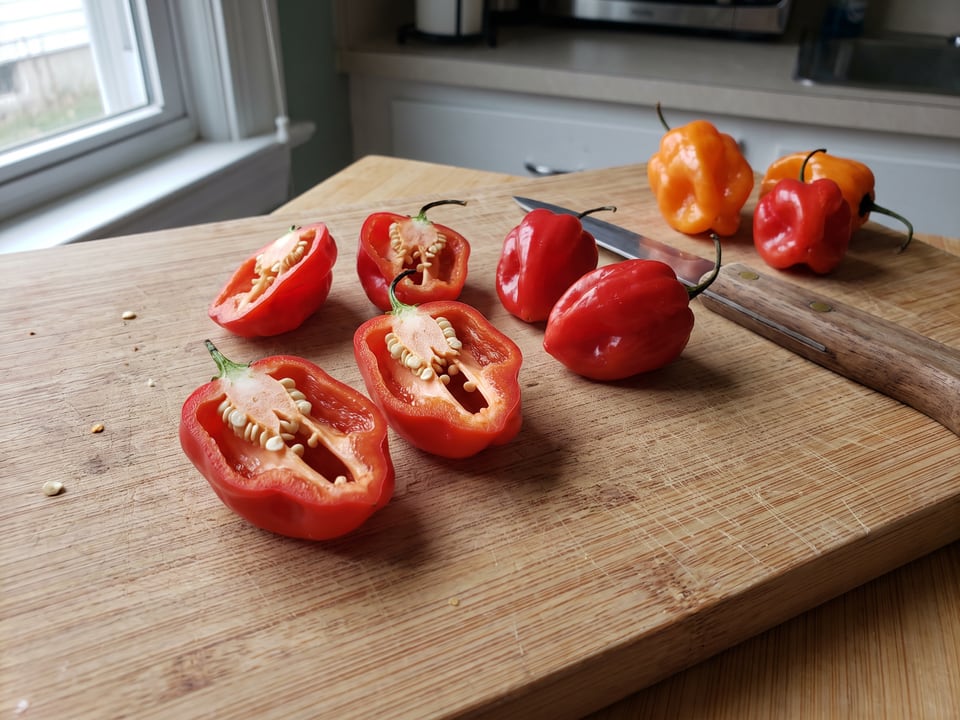 A Aji Dulce pepper cut open lengthwise beside a whole pod, showing the wall and seed cavity