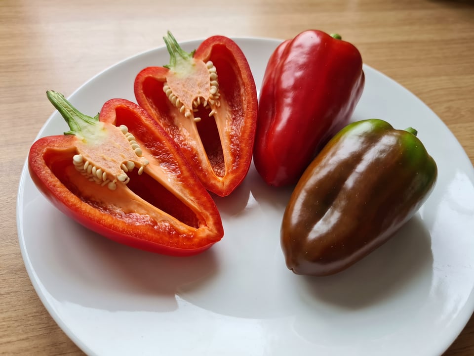 A Ancho San Luis pepper cut open lengthwise beside a whole pod, showing the wall and seed cavity
