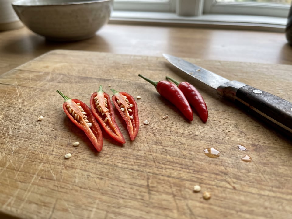 A Birdseye Chili pepper cut open lengthwise beside a whole pod, showing the wall and seed cavity