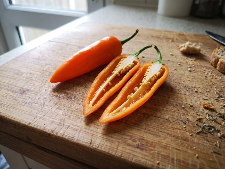 A Bulgarian Carrot pepper cut open lengthwise beside a whole pod, showing the wall and seed cavity