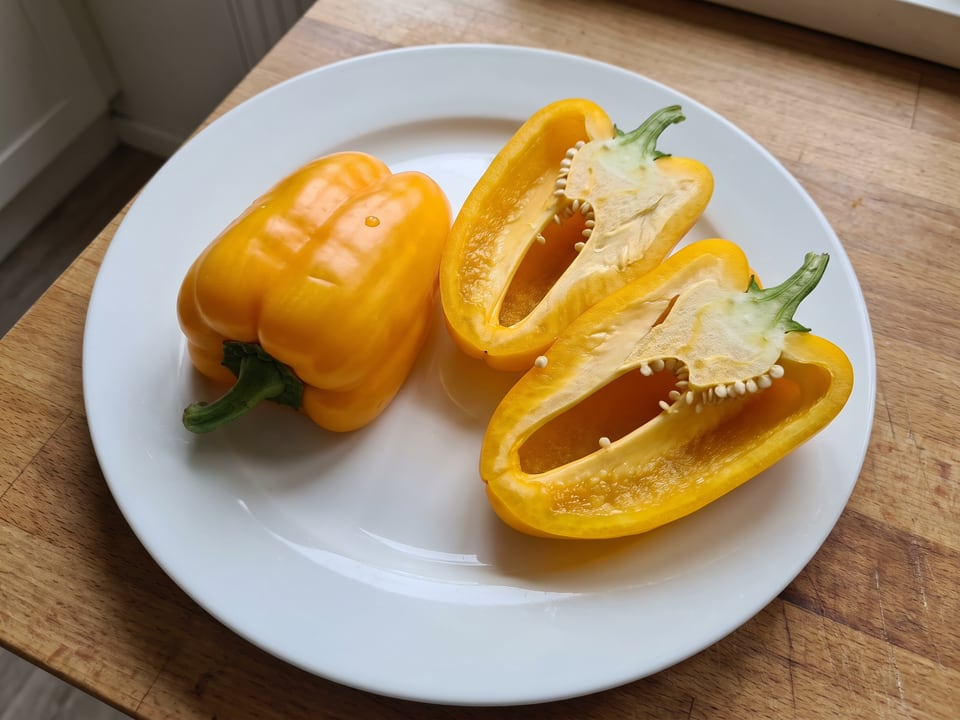 A Canary Bell pepper cut open lengthwise beside a whole pod, showing the wall and seed cavity