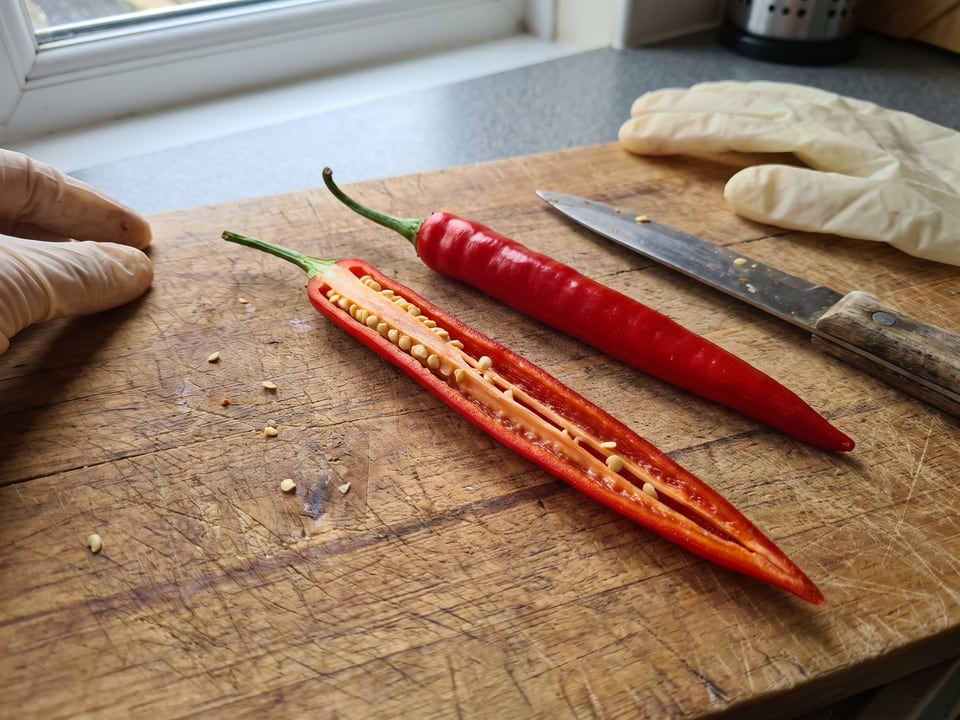A Cayenne Long Slim pepper cut open lengthwise beside a whole pod, showing the wall and seed cavity