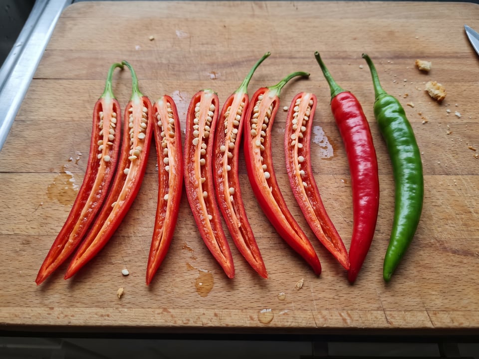 A Chile de Arbol pepper cut open lengthwise beside a whole pod, showing the wall and seed cavity