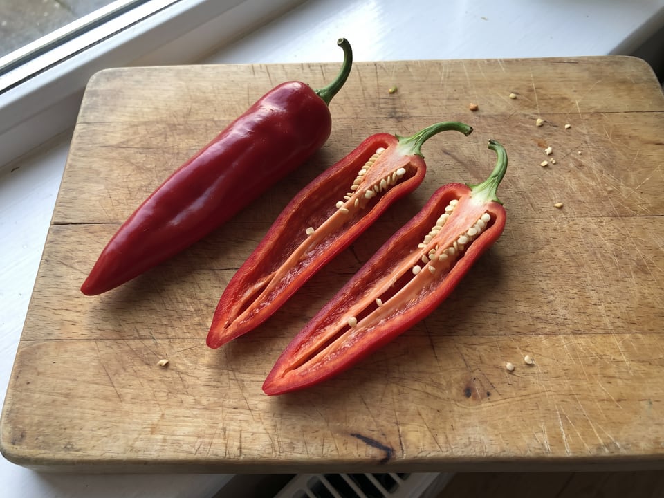 A Chimayo pepper cut open lengthwise beside a whole pod, showing the wall and seed cavity