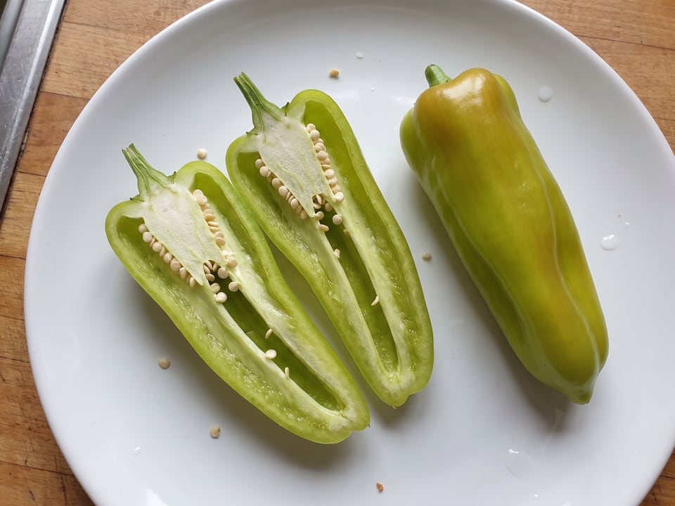 A Cubanelle pepper cut open lengthwise beside a whole pod, showing the wall and seed cavity
