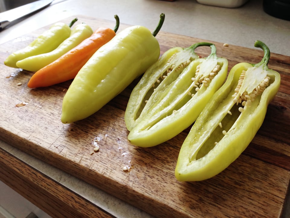 A Hungarian Yellow Wax pepper cut open lengthwise beside a whole pod, showing the wall and seed cavity