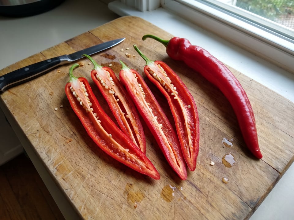A Jimmy Nardello pepper cut open lengthwise beside a whole pod, showing the wall and seed cavity