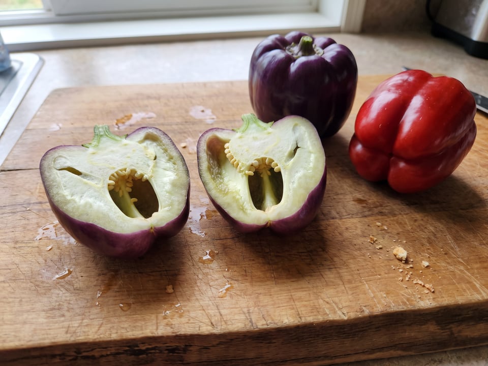 A Lilac Bell pepper cut open lengthwise beside a whole pod, showing the wall and seed cavity