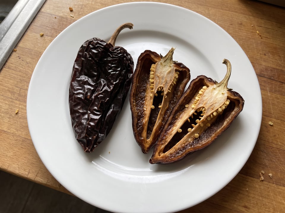 A Mulato Isleño pepper cut open lengthwise beside a whole pod, showing the wall and seed cavity