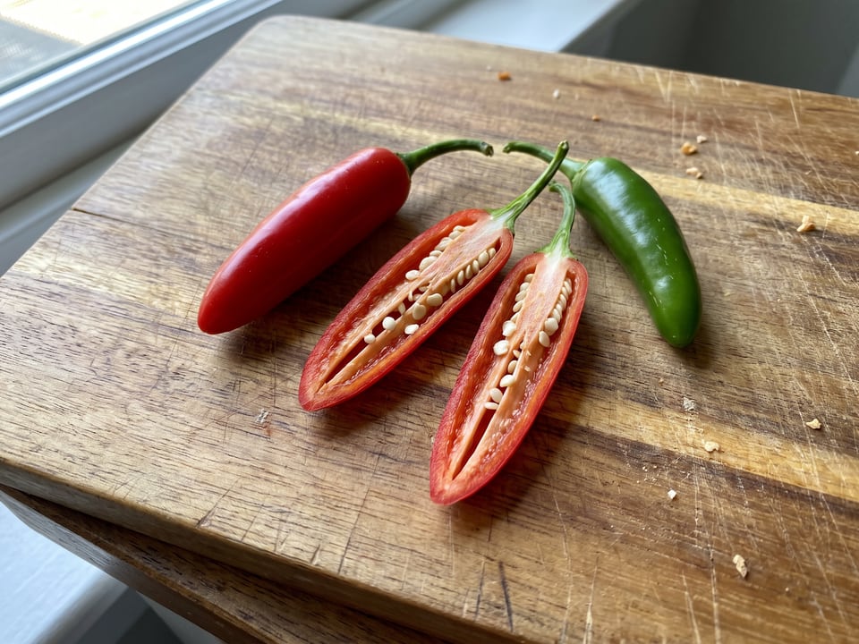 A Serrano Tampiqueño pepper cut open lengthwise beside a whole pod, showing the wall and seed cavity