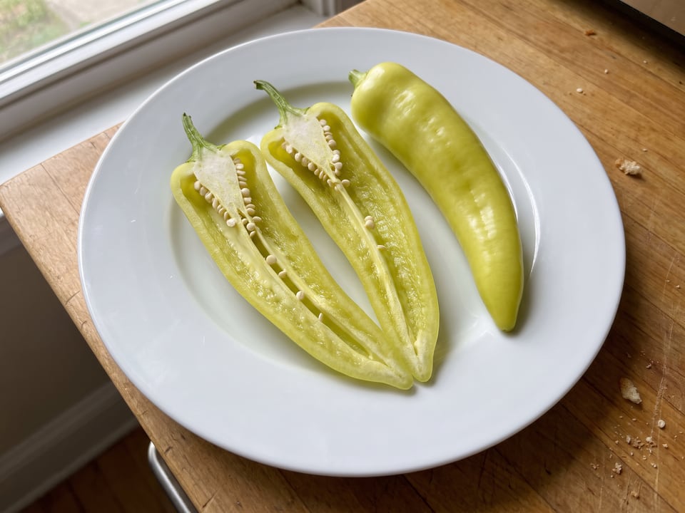 A Sweet Banana pepper cut open lengthwise beside a whole pod, showing the wall and seed cavity