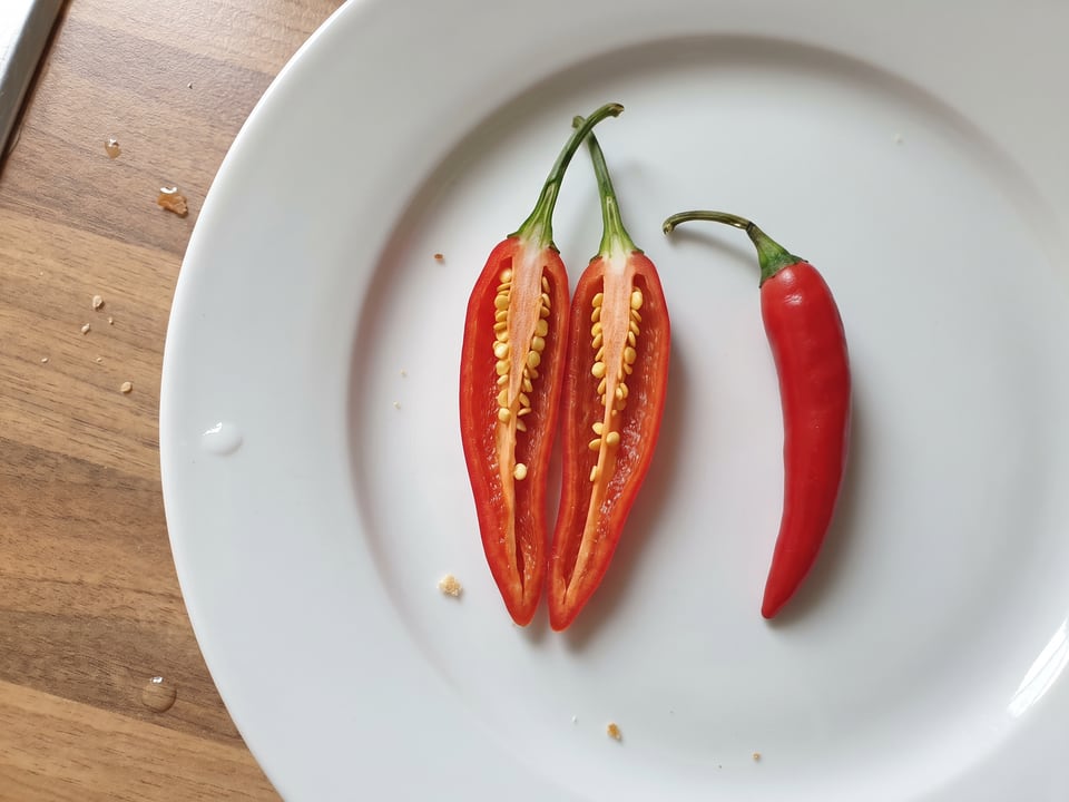 A Tabasco pepper cut open lengthwise beside a whole pod, showing the wall and seed cavity